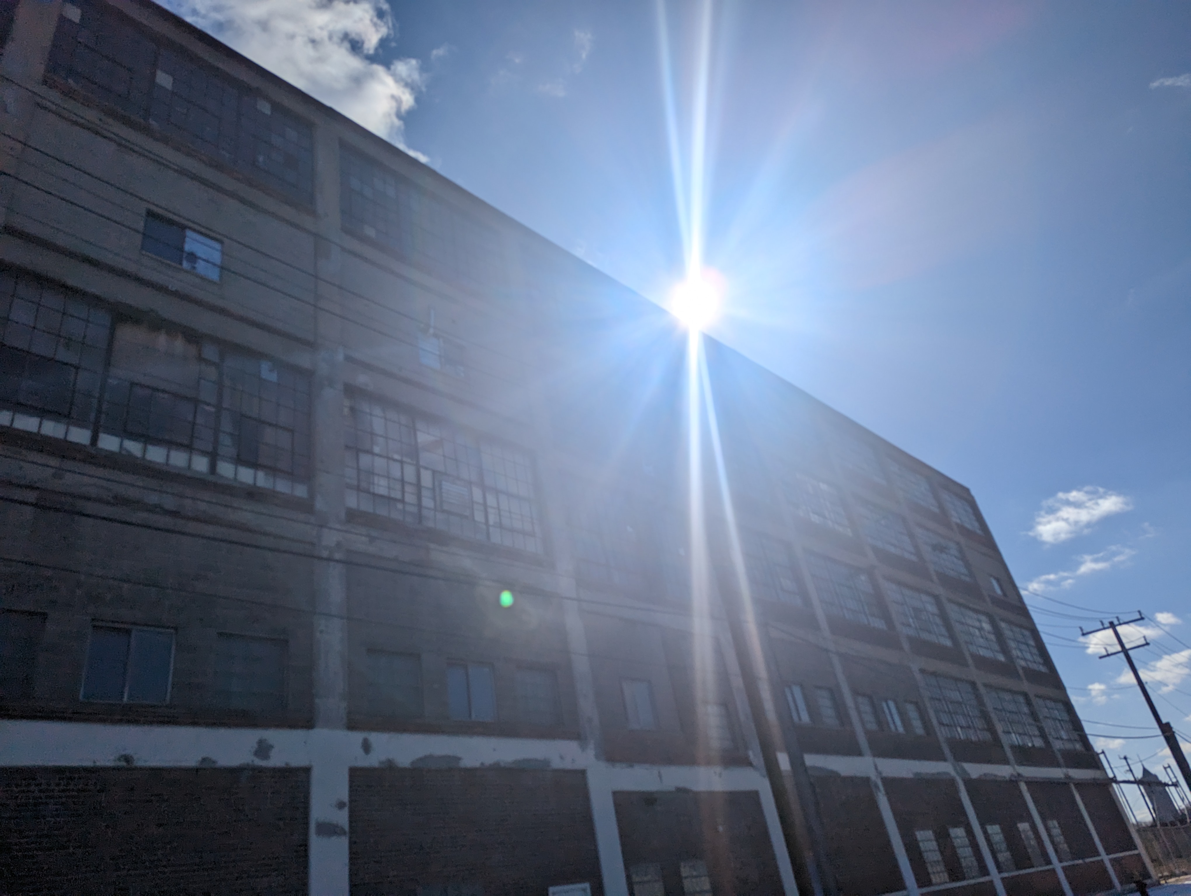 An image of the sun sending rays of light over a brick building in downtown Detroit.