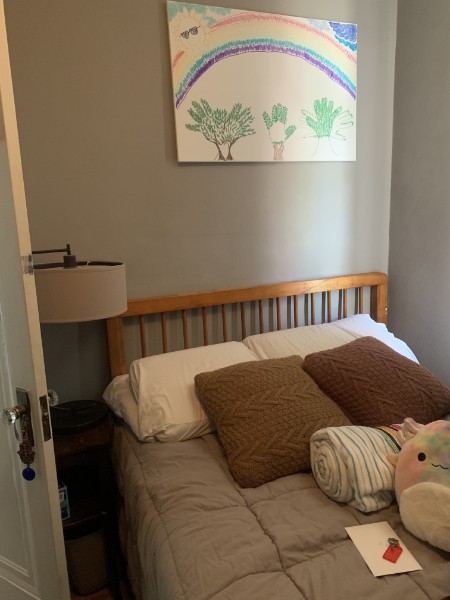 a comfy bed with a colorful drawing above it in a cozy room