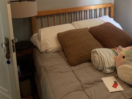 a cozy bed with pillows, a rainbow squishmallow, and blankets