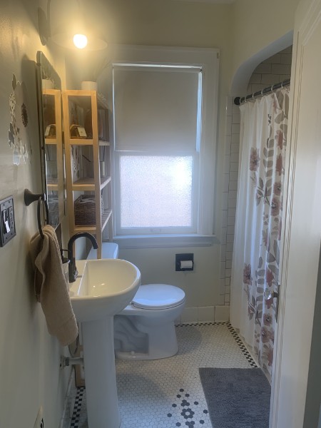 a clean bathroom with light streaming in from a window including toilet, sink, and shower curtain
